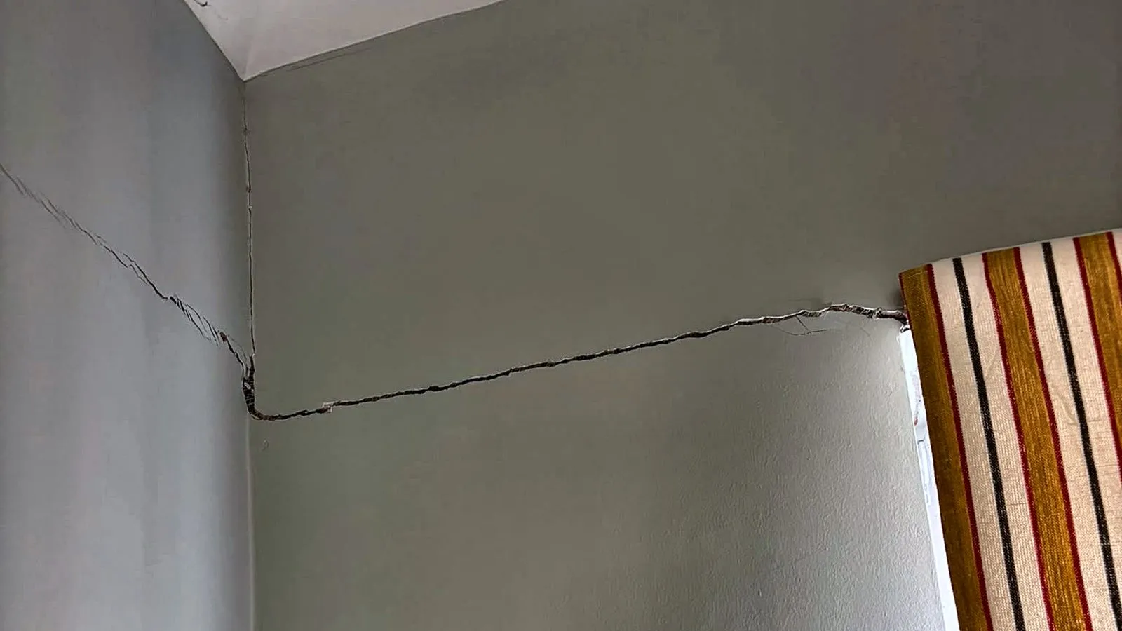 A wide crack running from the top of a window across a bedroom wall and round the corner towards the ceiling