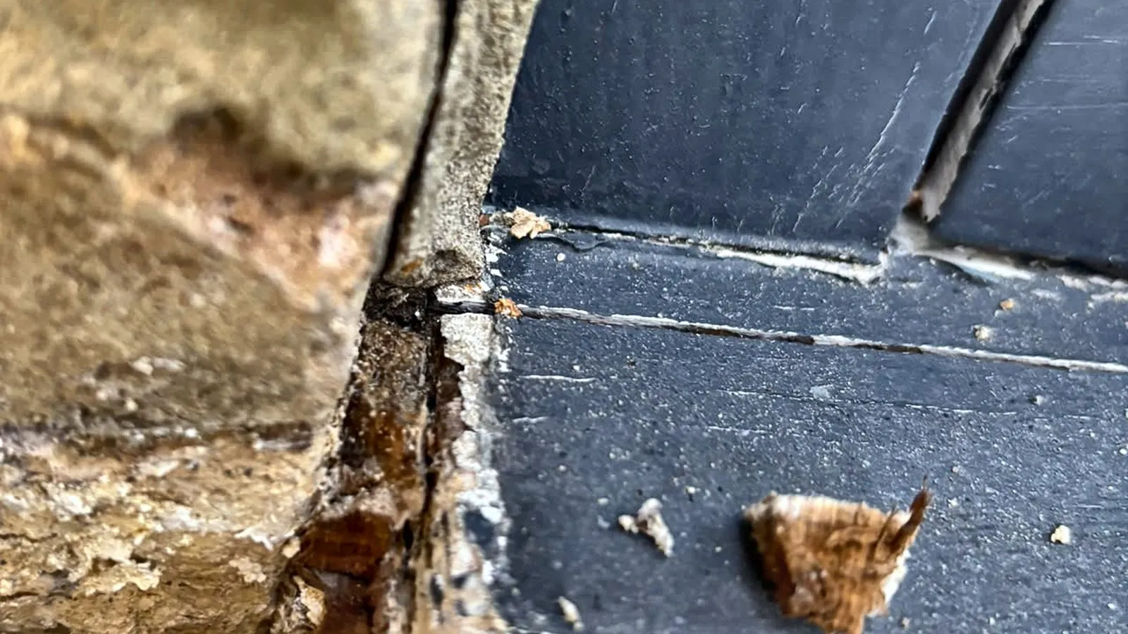 Rotten timber at the corner of a painted window frame where it meets the brickwork, with the joint opened up