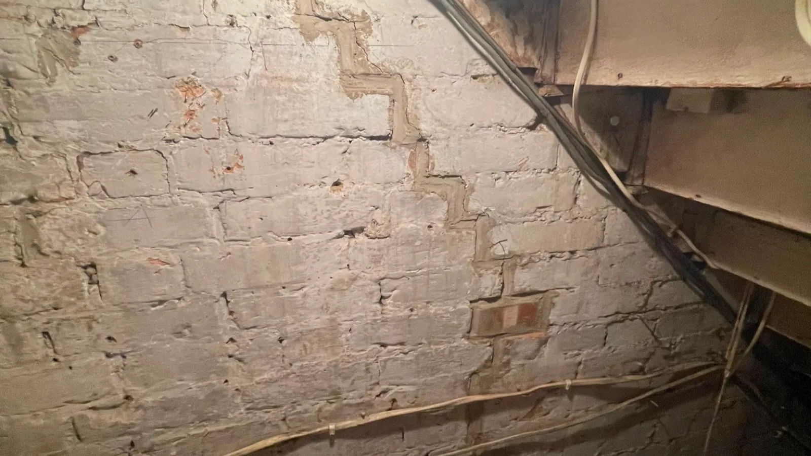 Stepped diagonal crack through the mortar joints of a painted brick wall