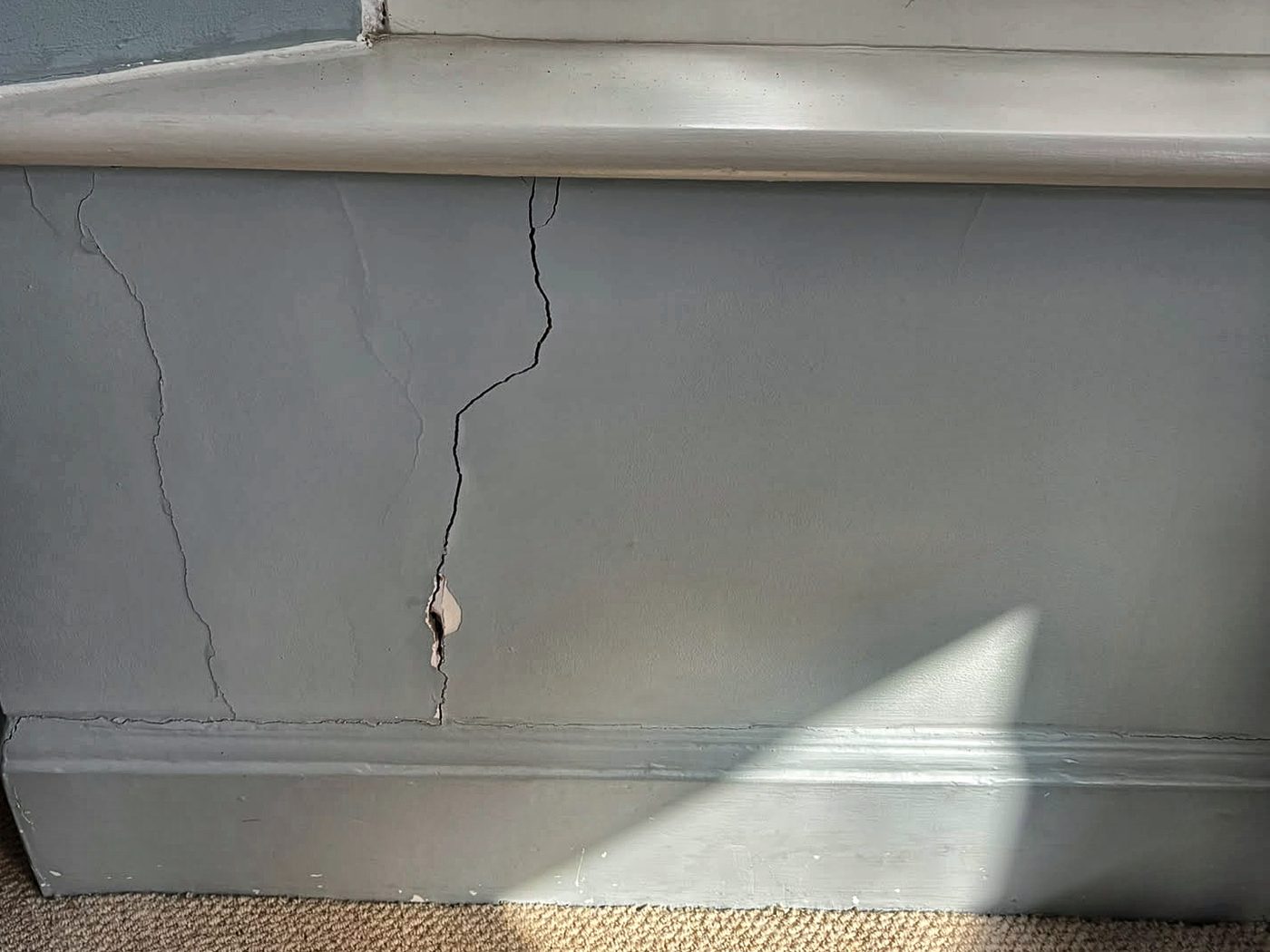 Two cracks in the plaster under a window board running down to the skirting, with a small piece of plaster broken away