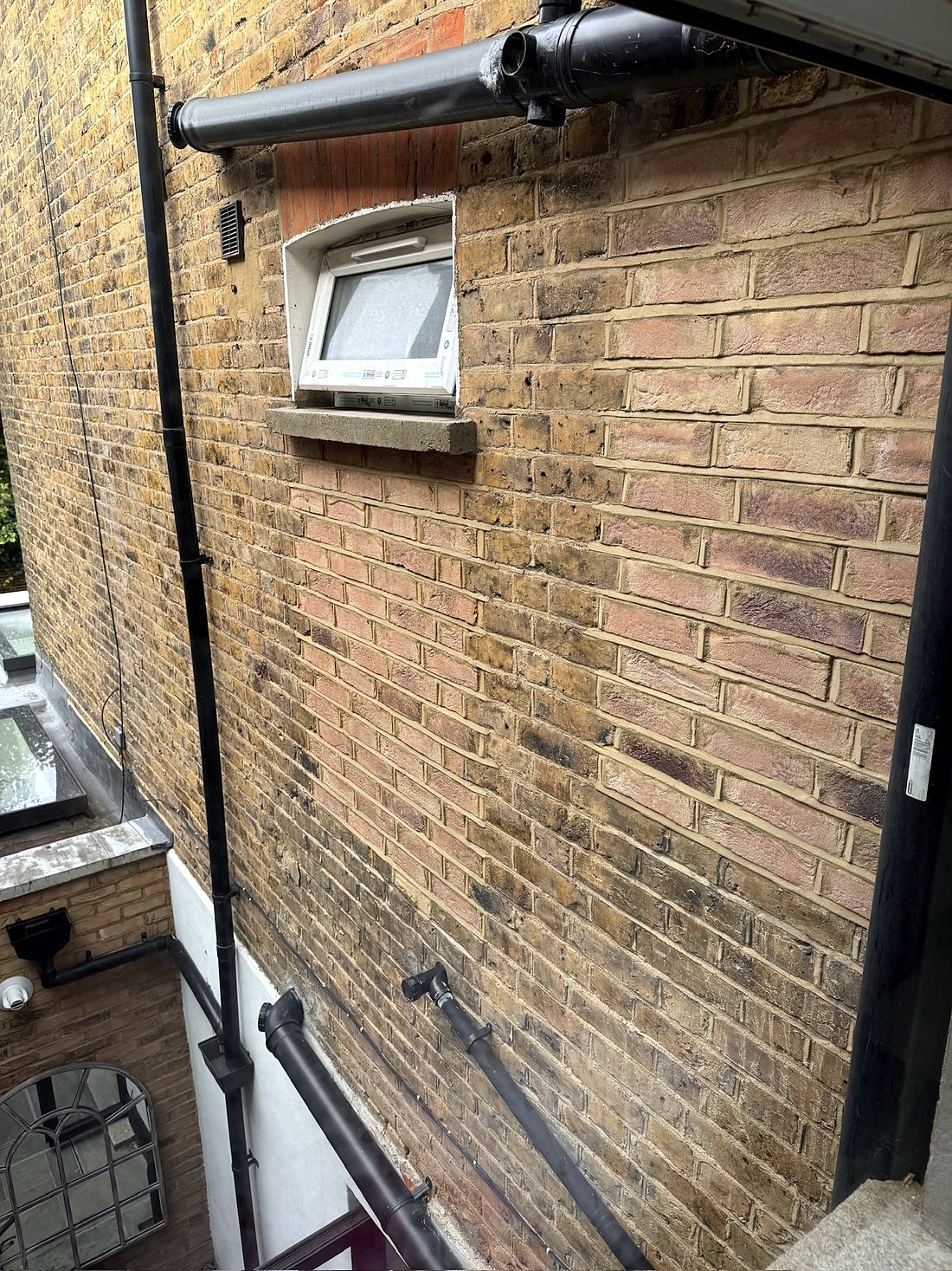 Rear wall of a London stock brick house with a small new uPVC window under an old red brick arch, and newer, pinker brickwork with fresh pointing below and to the right of it